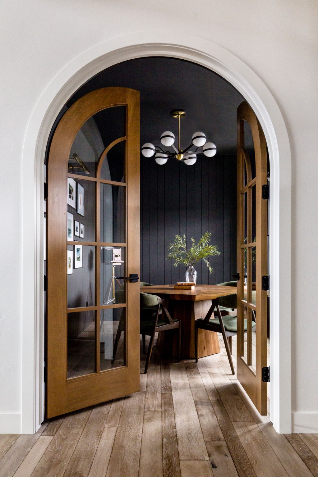Finished arched doorway framing a deep charcoal dining room with warm wood doors and crisp white trim